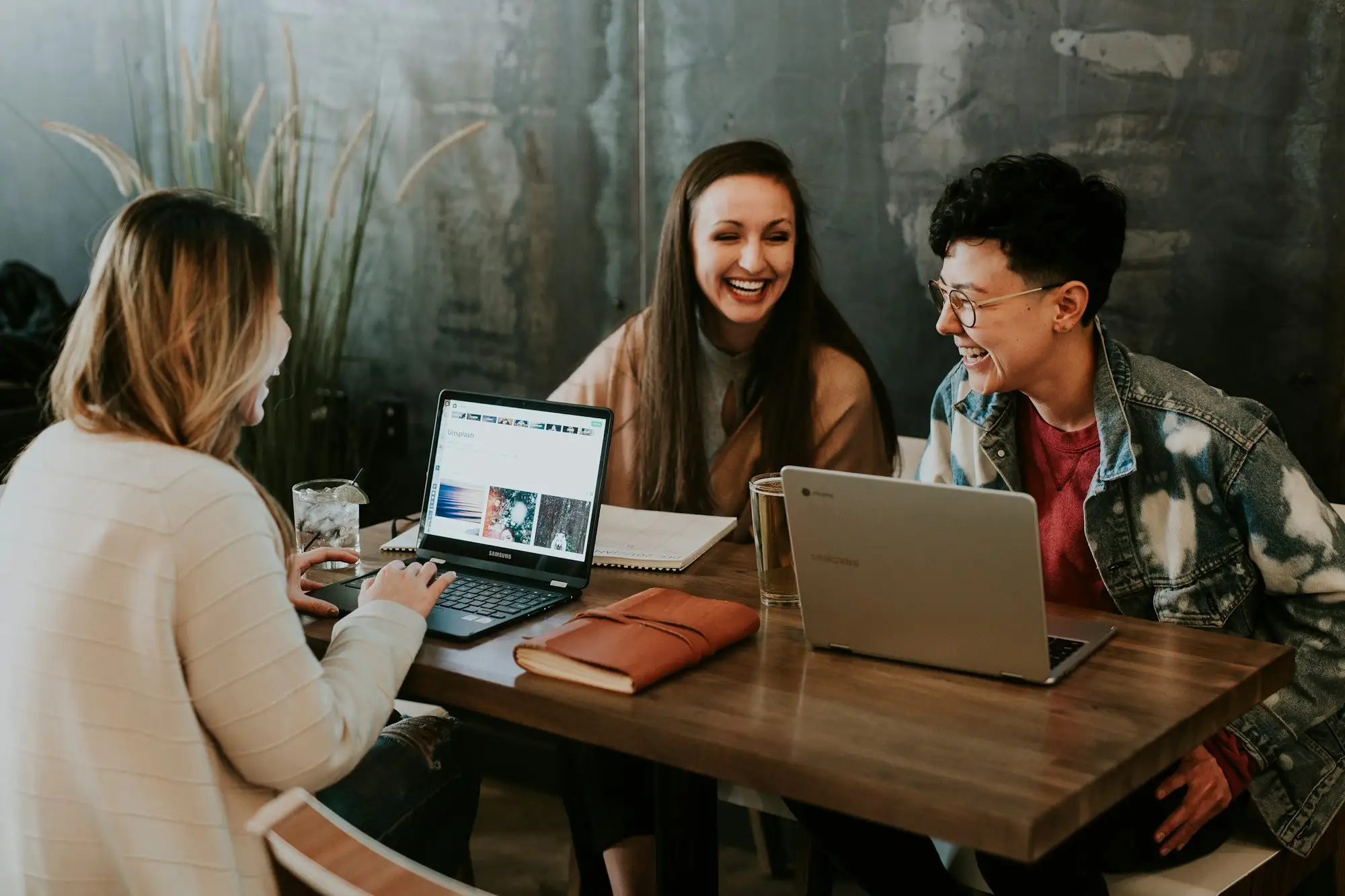Three people laughing together in front of their laptops
